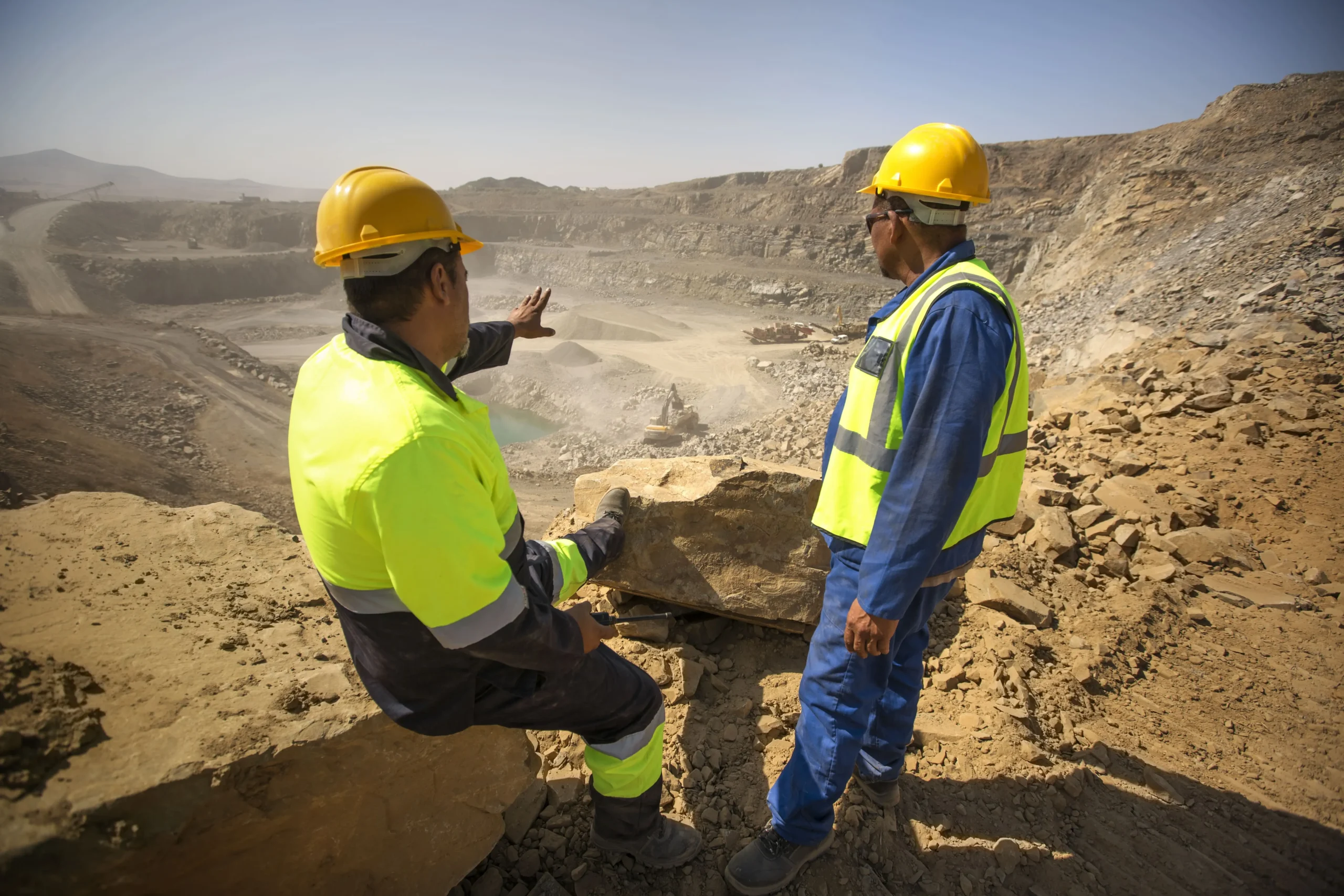 Dos operarios sentados sobre unas rocas señalando hacia una cantera